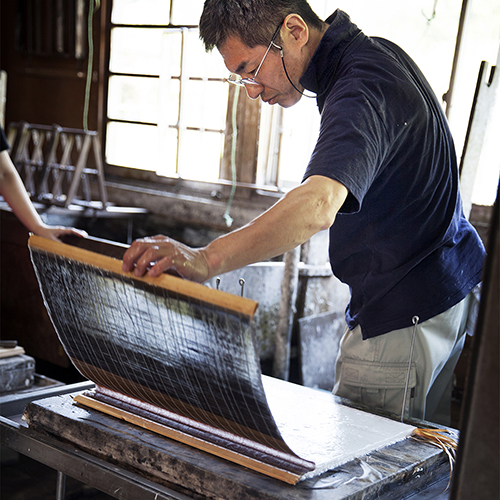 Japanese man holding a paper frame and inspecting fresh piece of traditional Washi paper.